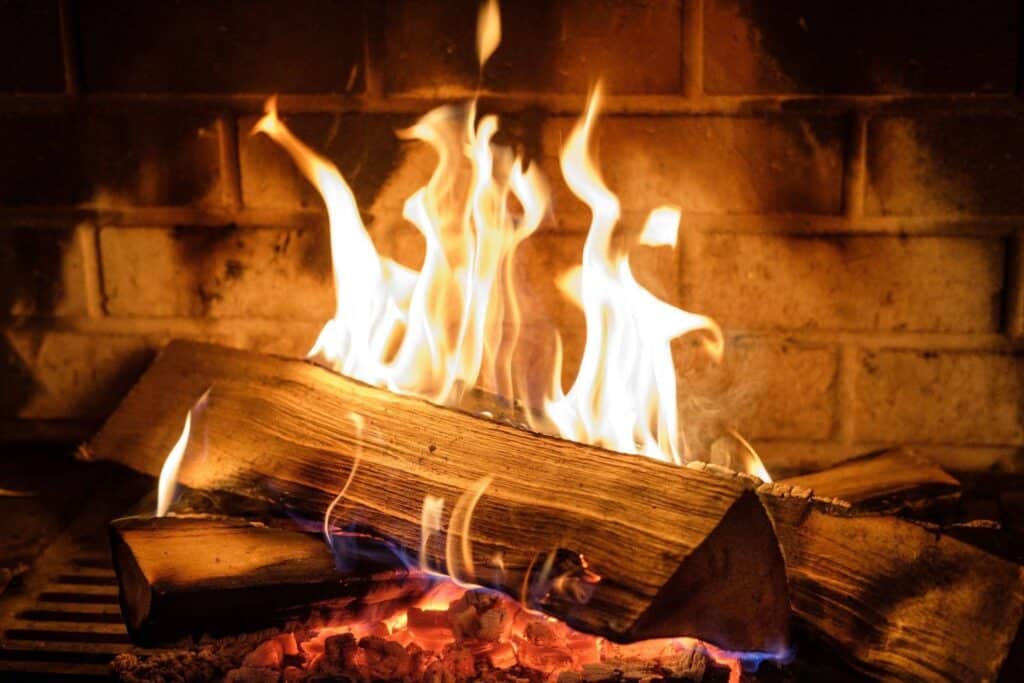 Flames flicker in a fireplace illuminating the logs arranged beneath them