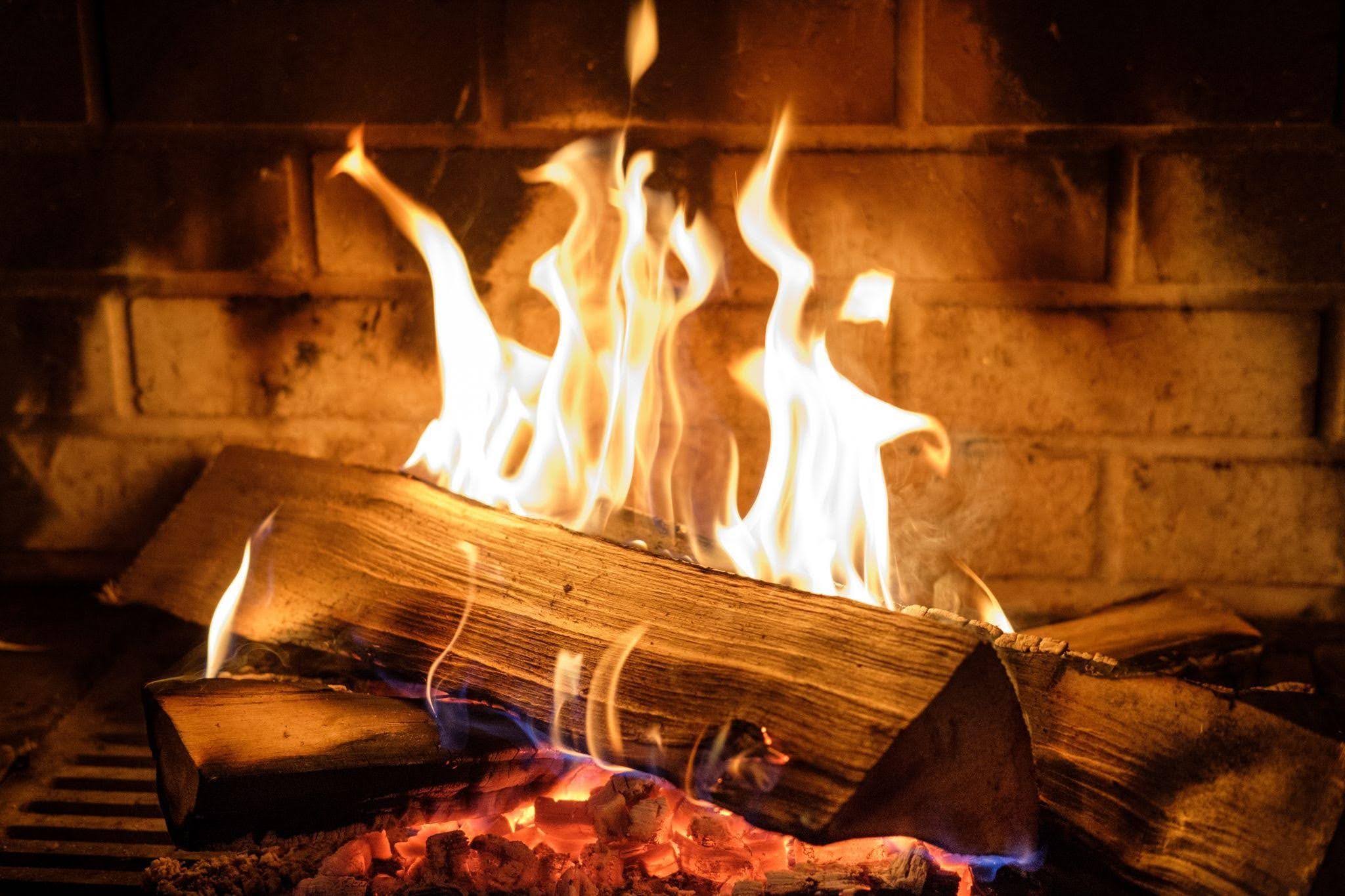 Flames flicker in a fireplace illuminating the logs arranged beneath them