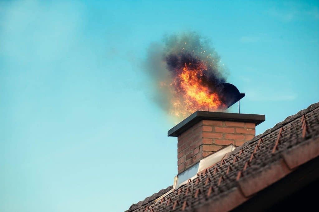 A chimney with flames and smoke billowing out indicating a fire burning inside the fireplace