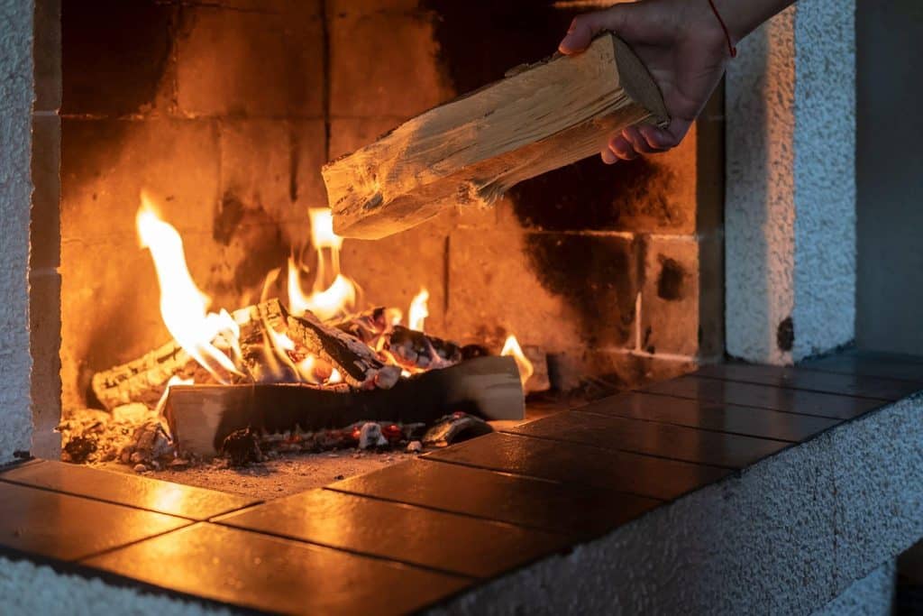 A person grips a wooden log above a campfire flames flickering in the background creating a warm glow
