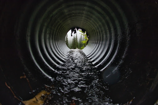 A man standing in the middle of a pipe in a canal.

