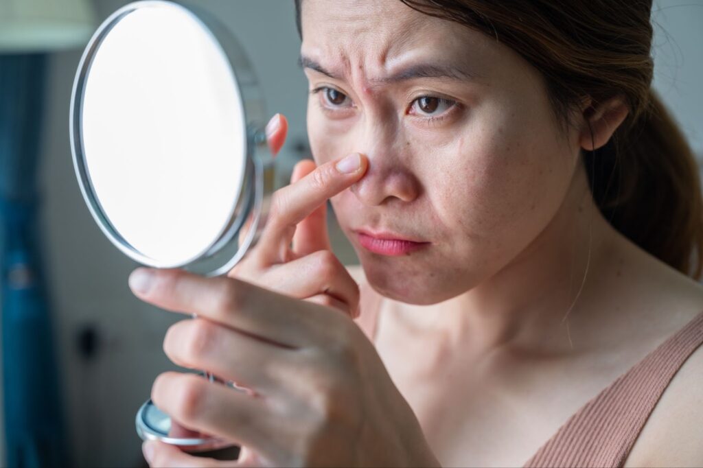 A woman examining her nose in the mirror.