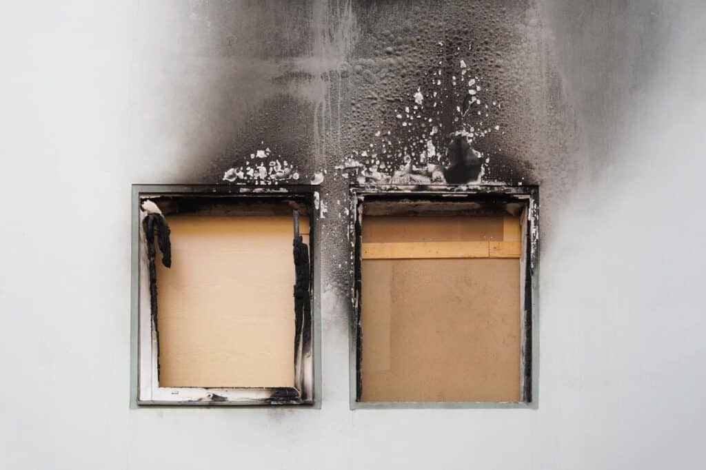 Smoke billows from two windows emphasizing the need for smoke damage restoration to prevent further damage in your home.