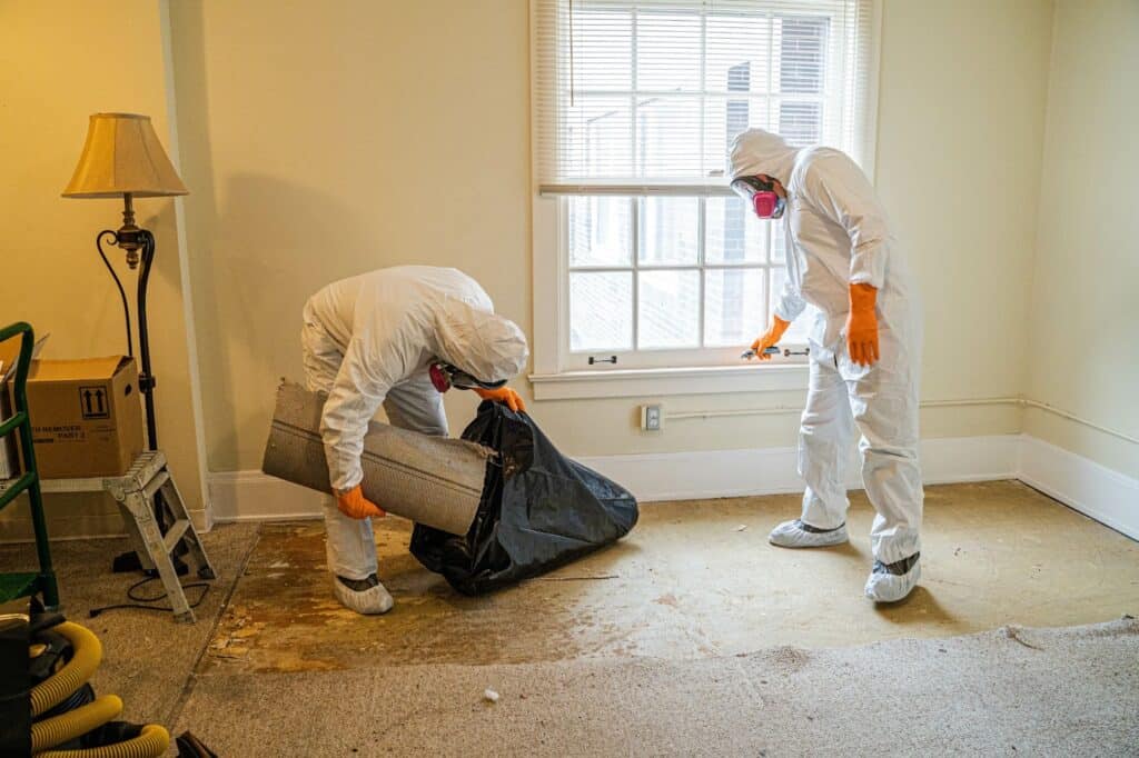 Two men in protective gear and masks carrying out mold removal, restoration, and prevention work in a room