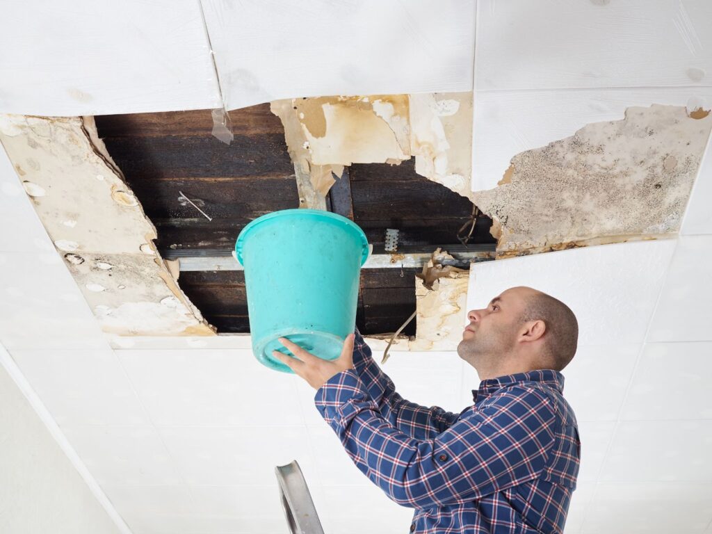 Man cleaning ceiling with bucket for water damage remediation and restoration services