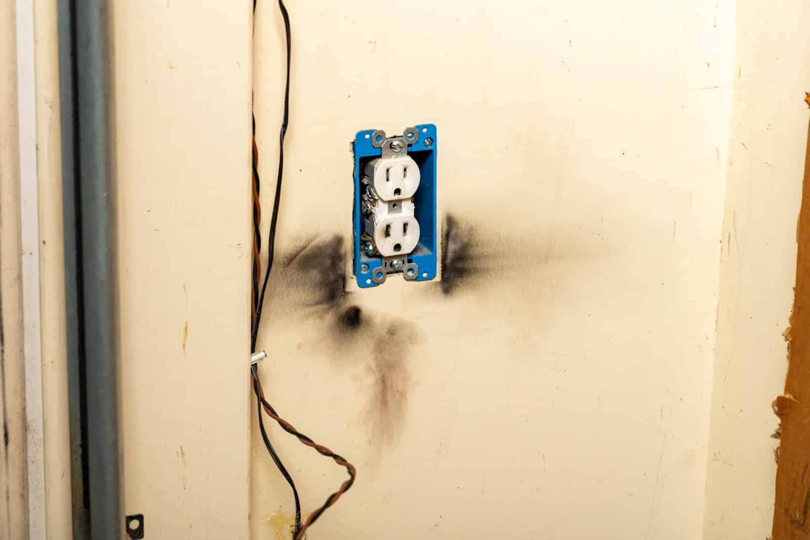 A wall with a blue outlet and a black electrical box, showing smoke damage, in need of smoke damage restoration.
