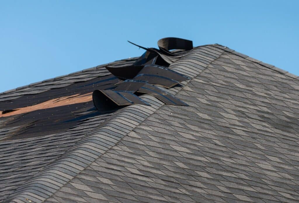 A roof with damaged shingles and a broken window, highlighting the effects of wind damage requiring cleanup and restoration.