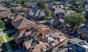 Aerial view of a neighborhood showing debris and damaged roofs, highlighting the need for cleanup and restoration efforts.