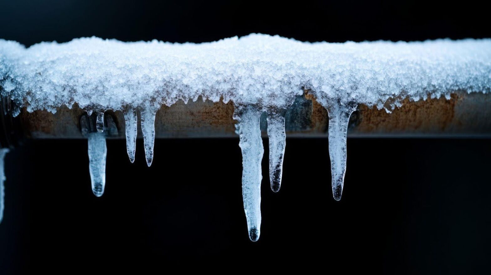 Icicles hang from a pipe against a black background, showcasing intricate shapes