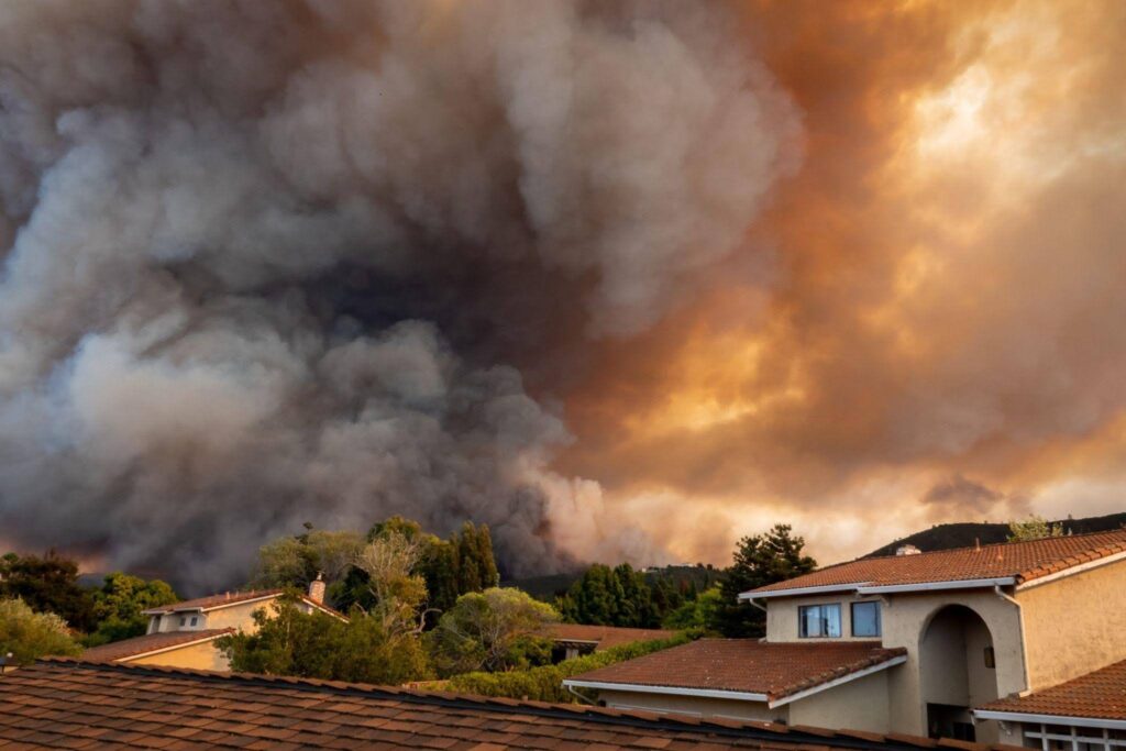 A view of a wildfire burning in the distance captured from the roof of a house with smoke billowing into the sky